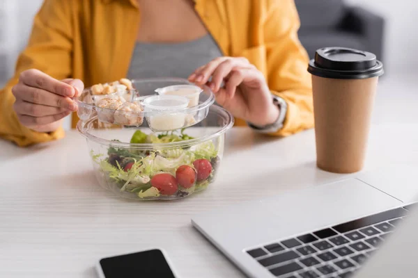 Partial view of teleworker near fresh salad, coffee to go and gadgets on blurred foreground — Stock Photo