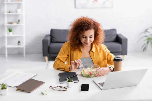 Молодий фрілансер їсть свіжий салат біля ноутбука вдома — стокове фото