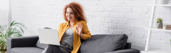 Mulher alegre ter vídeo chat no laptop e mão acenando no sofá, banner — Fotografia de Stock