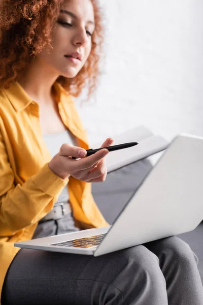 Junge Freiberuflerin zeigt mit Stift auf Laptop, verschwommener Hintergrund — Stockfoto