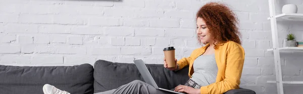 Donna gioiosa seduta sul divano con caffè per andare e laptop, banner — Foto stock