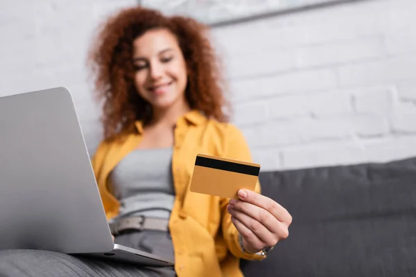 Selective focus of credit card in hand of woman with laptop on blurred background — Stock Photo