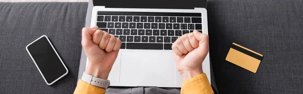 Vista ritagliata della donna con pugni stretti vicino al computer portatile, smartphone con schermo bianco e carta di credito, banner — Foto stock