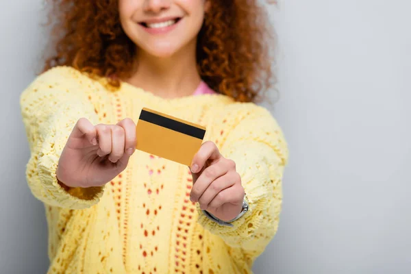 Cropped view of smiling woman showing credit card on grey, blurred background — Stock Photo