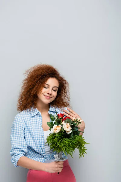 Erfreut Frau mit lockigem Haar hält Blumen auf grauem Hintergrund — Stockfoto