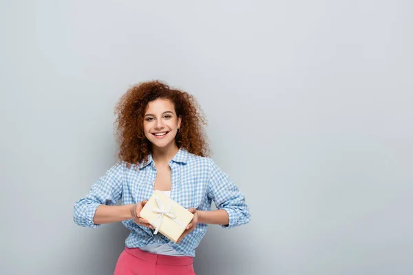 Happy woman looking at camera while holding present on grey background — Stock Photo