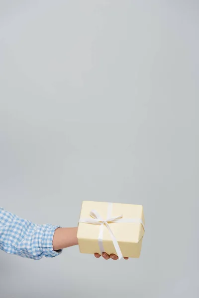 Partial view of woman holding gift box with white ribbon isolated on grey — Stock Photo