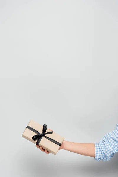 Cropped view of woman holding gift box with black ribbon on grey background with copy space — Stock Photo
