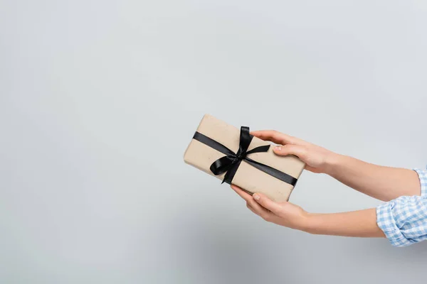 Partial view of woman holding gift box with black ribbon on grey background — Stock Photo