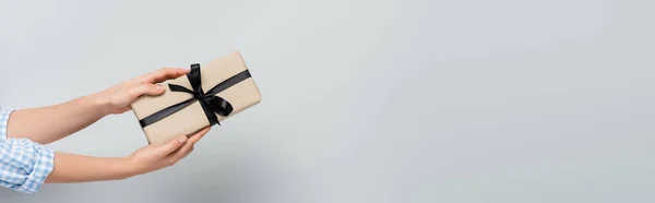 Partial view of woman holding gift box with black ribbon on grey background, banner — Stock Photo