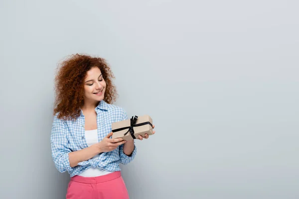 Mujer feliz en camisa a cuadros sosteniendo presente sobre fondo gris - foto de stock