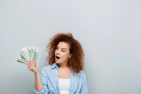 Femme excitée en chemise à carreaux regardant les billets en dollars isolés sur gris — Photo de stock