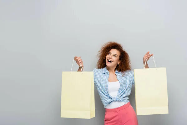 Mujer asombrada mirando hacia otro lado mientras sostiene compras sobre fondo gris - foto de stock