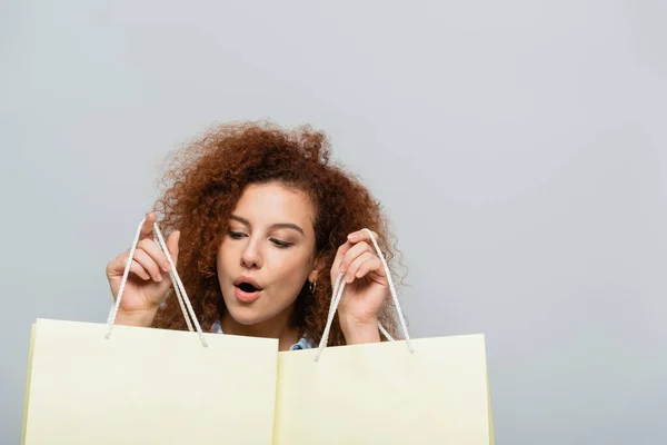 Mujer asombrada con la boca abierta sosteniendo bolsas aisladas en gris - foto de stock