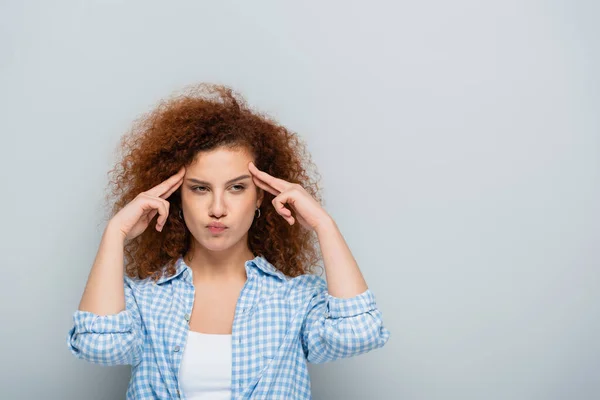 Ernste Frau mit welligem Haar, die den Kopf berührt, während sie isoliert in grau denkt — Stockfoto