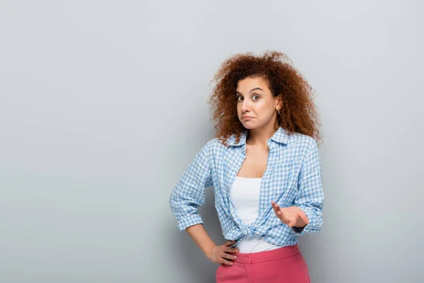 Discouraged woman pointing with hand while looking at camera on grey background — Stock Photo