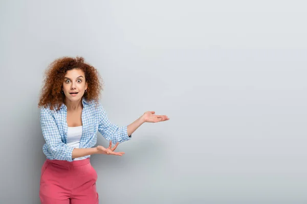 Astonished woman pointing with hands while looking at camera on grey background — Stock Photo