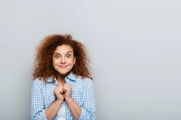 Mujer positiva mostrando el gesto de la suerte con los puños cerrados aislados en gris - foto de stock