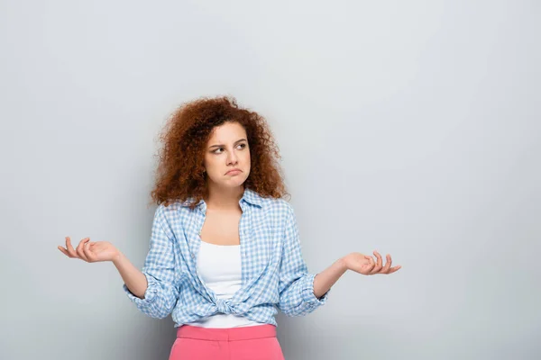 Mujer confundida mostrando gesto de encogimiento mientras mira hacia otro lado sobre fondo gris - foto de stock