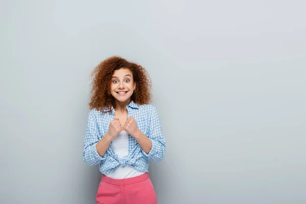 Mujer asombrada mostrando gesto de suerte mientras mira a la cámara sobre fondo gris - foto de stock