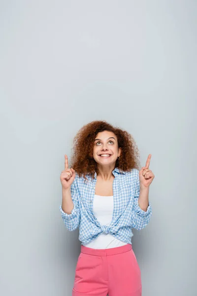 Excited woman looking up and pointing with fingers on grey background — Stock Photo