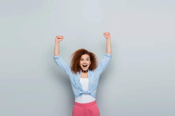 Astonished woman with curly hair showing rejoice gesture on grey background — Stock Photo