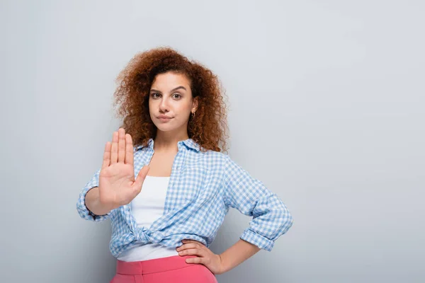 Mujer disgustada mostrando gesto de rechazo mientras está de pie con la mano en la cadera sobre fondo gris - foto de stock