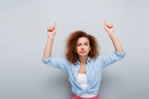 Serious woman pointing up with fingers while looking at camera on grey background — Stock Photo