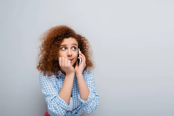 Confusa donna guardando altrove mentre parla su smartphone isolato su grigio — Foto stock