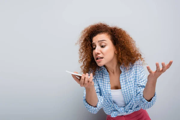 Irritierte Frau gestikuliert beim Senden von Sprachnachrichten auf Handy auf grauem Hintergrund — Stockfoto