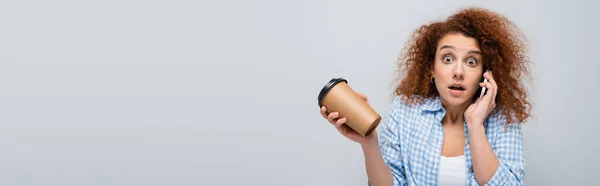 Mulher chocada segurando café para ir enquanto fala no celular isolado em cinza, banner — Fotografia de Stock