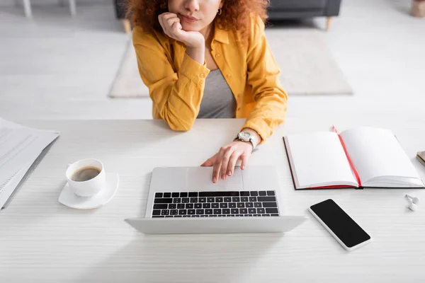 Vue partielle du télétravailleur près de l'ordinateur portable, téléphone portable avec écran vierge et ordinateur portable vide sur le bureau — Photo de stock