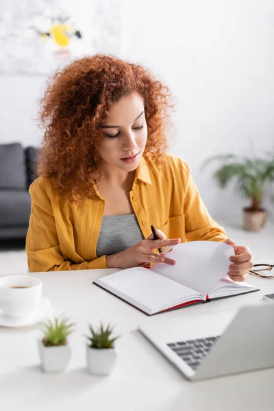 Junge Freiberuflerin arbeitet mit Notebook in Laptopnähe im unscharfen Vordergrund — Stockfoto