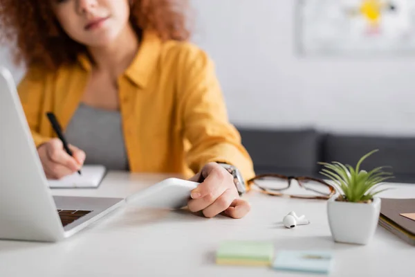 Cropped view of freelancer with smartphone working near laptop on blurred background — Stock Photo