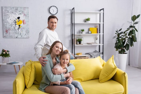 Smiling woman hugging kid near husband at home — Stock Photo