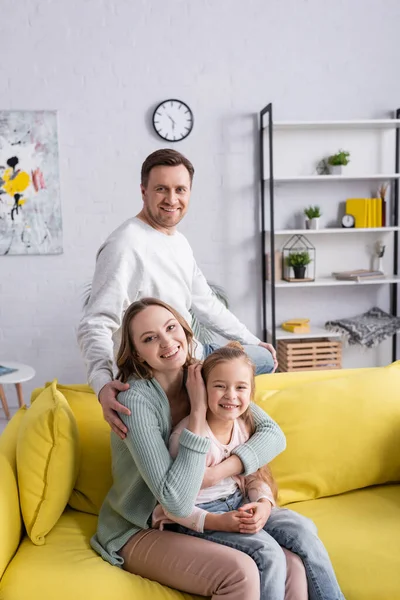 Cheerful man looking at camera near wife hugging daughter — Stock Photo