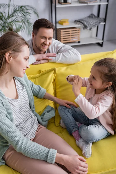 Smiling woman looking at child near blurred husband on couch — Stock Photo