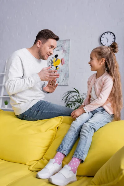 Homme parlant à une fille souriante assis sur le canapé — Photo de stock