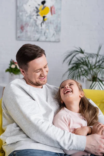 Мужчина обнимает позитивного ребенка на диване — стоковое фото