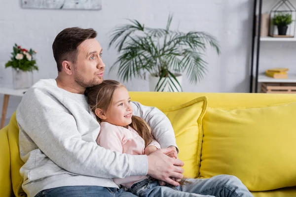 Man talking while hugging smiling child on couch — Stock Photo