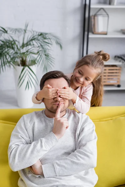 Smiling kid covering eyes of father showing secret gesture — Stock Photo