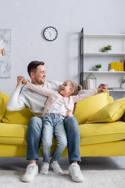 Padre sorridente che si tiene per mano di figlia sul divano — Foto stock