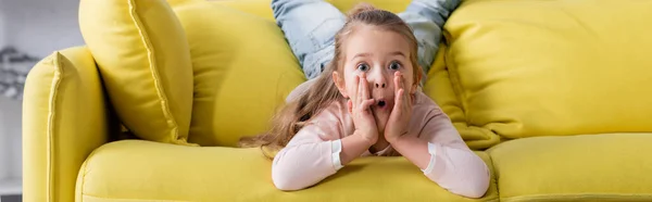 Amazed child looking at camera on sofa, banner — Stock Photo