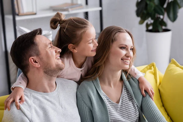 Lächelndes Mädchen umarmt Eltern auf gelber Couch — Stockfoto