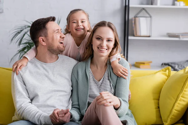 Kid embracing happy parents on sofa at home — Stock Photo