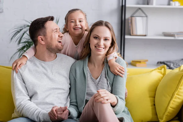 Niño abrazando feliz padres en sofá en casa - foto de stock