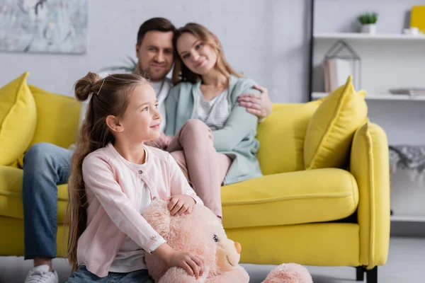 Positives Kind hält Stofftier in der Nähe der Eltern auf verschwommenem Hintergrund — Stockfoto