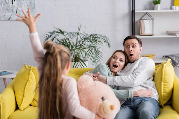 Erstaunte Eltern schauen Kind mit Teddybär im verschwommenen Vordergrund an — Stockfoto