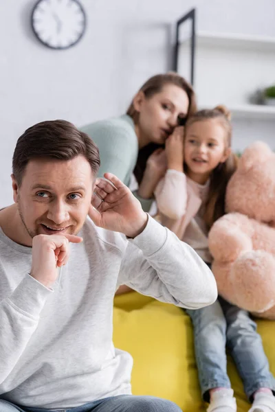 Sonriente hombre escuchando cerca de esposa e hija con juguete suave sobre fondo borroso - foto de stock