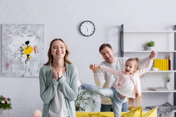 Cheerful woman standing near family having fun on blurred background — Stock Photo